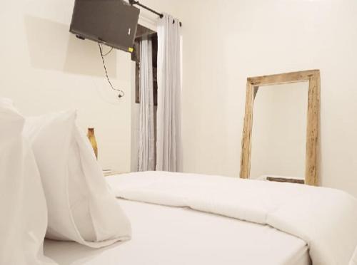 1 cama blanca con almohadas blancas y espejo en Classic Local House Grenceng, en Denpasar