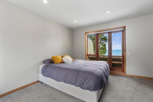 a bedroom with a bed and a large window at Beachside Luxury - Laingholm Holiday Apartment in Titirangi