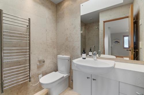 Baño blanco con aseo y lavamanos en Beachside Luxury - Laingholm Holiday Apartment en Titirangi