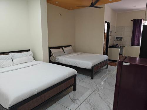 a bedroom with two beds and a kitchen in the background at Comfort Cove Apartments in Mysore