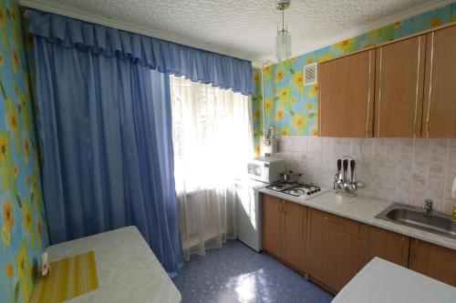 - une cuisine avec une fenêtre dotée de rideaux bleus et d'un évier dans l'établissement Катюша, à Petropavlovsk-Kamtchatski