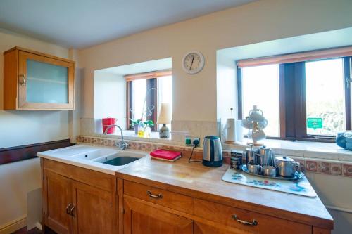 uma cozinha com um balcão e um lavatório e duas janelas em Midsummer Barn em Darwen