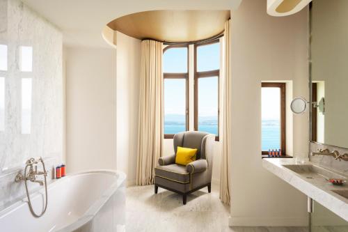 a bathroom with a tub and a chair with a window at Hôtel Royal in Évian-les-Bains