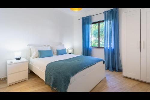 Schlafzimmer mit einem Bett mit blauen Vorhängen und einem Fenster in der Unterkunft Falésia Modern Flat W/Balcony & Pool by LovelyStay in Albufeira