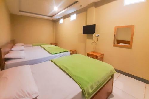 two beds in a room with a tv on the wall at Delvia Bromo Homestay Mitra RedDoorz in Pasuruan
