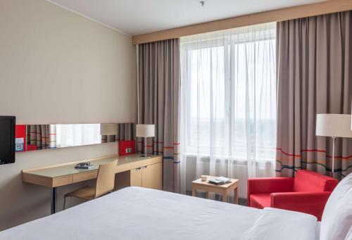 a hotel room with a bed and a desk and a red chair at Cosmos Yaroslav Hotel, a member of Radisson Individuals in Yaroslavl