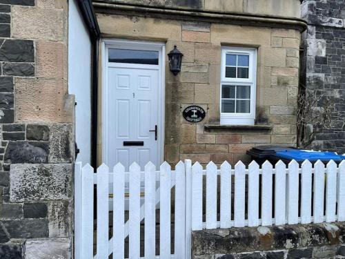 a white picket fence in front of a house with a white door at Crossways Cottage Quirky 2 bedroom cottage in Damdale, Central Peebles in Peebles