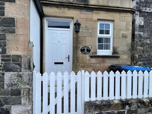 a white picket fence in front of a house with a white door at Crossways Cottage Quirky 2 bedroom cottage in Central location in Peebles