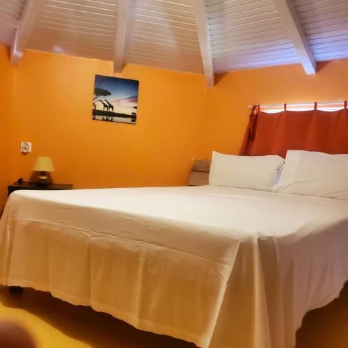 a bedroom with a large white bed with orange walls at Bungalow de 2 chambres avec piscine partagee jacuzzi et terrasse amenagee a Le Gosier a 5 km de la plage in Le Gosier