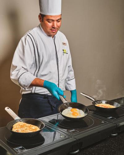 a chef cooking eggs in a pan on a stove at Triumph White Sands Hotel in Marsa Matruh