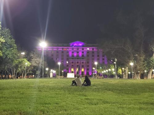 deux personnes assises dans l'herbe devant un bâtiment aux lumières violettes dans l'établissement Departamento Barrio Cívico, à Mendoza