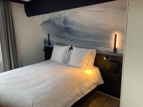 a bedroom with a white bed with a painting on the wall at Hotel Dunepanne in De Haan