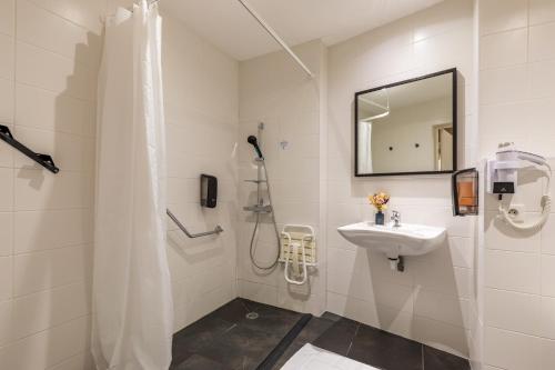 baño blanco con ducha y lavamanos en Hotel-Restaurant Le Victoria, en Rennes