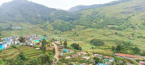 a village on a hill with mountains in the background at Misty Mountains Holiday Homes in Vattavada