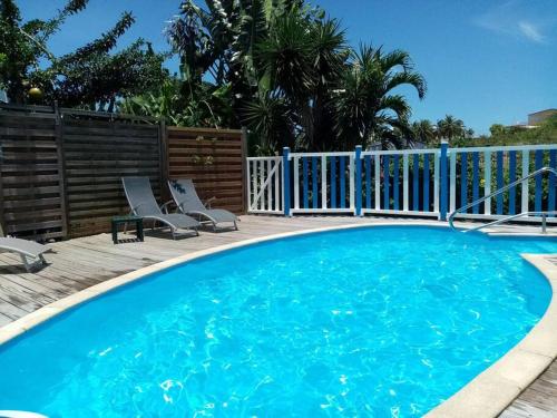 a large blue swimming pool with chairs and a fence at Bungalow papaye in Sainte-Anne