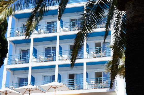Cet hôtel possède des balcons bleus et blancs et des palmiers. dans l'établissement Hôtel California, au Lavandou