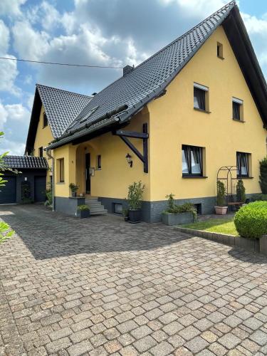 a yellow house with a brick driveway at Ferienwohnung Klatschmohn in Wallscheid