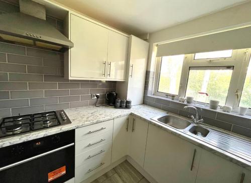 una cucina con armadi bianchi, lavandino e finestra di Modern Stylish Two Bedroom Apartment a Beckenham