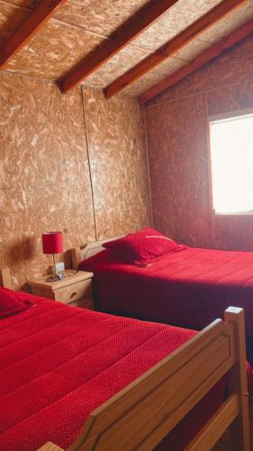 um quarto com 2 camas com lençóis vermelhos e uma janela em Ebenzer Comidas y Cabañas em Cochrane