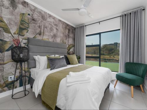 a bedroom with a large bed and a green chair at Ballito Village Luxury Apartments by DropInn in Ballito