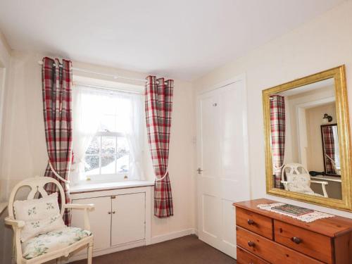 a room with a mirror and a chair and a dresser at Rose Cottage in Strathpeffer
