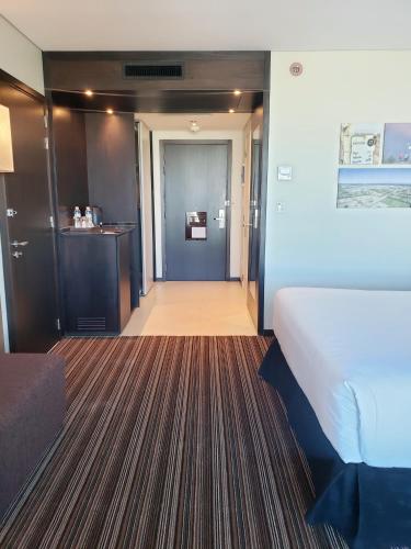 a hotel room with a bed and a corridor at Hilton Garden Inn Neuquen in Neuquén