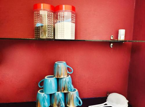 a shelf with cups and books on a red wall at Mannat Inn Homestay (Mysore) in Mysore