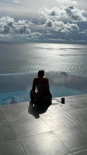 a man sitting on the ground next to a swimming pool at Villa Club Tropicana Carana with infinity pool in Machabee