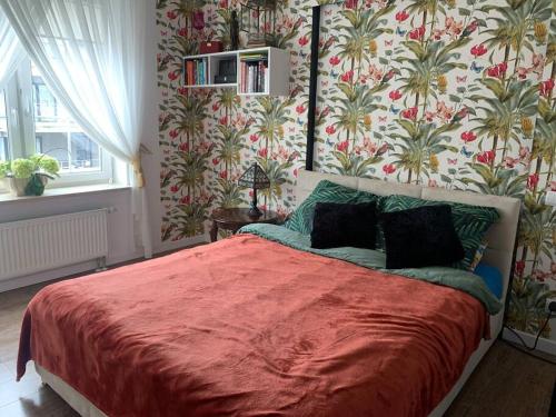 a bedroom with a bed with a red blanket and wallpaper at Przytulny apartament blisko plaży, z miejscem postojowym in Giżycko