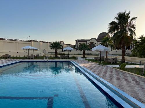 ein großer Pool mit Sonnenschirmen vor einem Gebäude in der Unterkunft Elphardous Oasis Hotel in Luxor