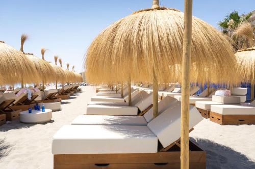 a row of beach chairs with straw umbrellas on the beach at Higuerón Hotel Curio Collection by Hilton in Fuengirola
