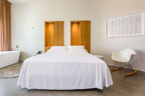 a white bedroom with a white bed and a chair at Higuerón Hotel Curio Collection by Hilton in Fuengirola