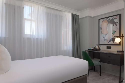a bedroom with a white bed and a desk and a window at DoubleTree By Hilton Brighton Metropole in Brighton & Hove