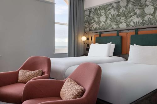 a hotel room with two beds and two chairs at DoubleTree By Hilton Brighton Metropole in Brighton & Hove