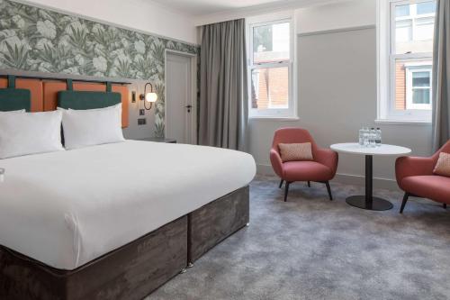 a bedroom with a bed and two chairs and a table at DoubleTree By Hilton Brighton Metropole in Brighton & Hove