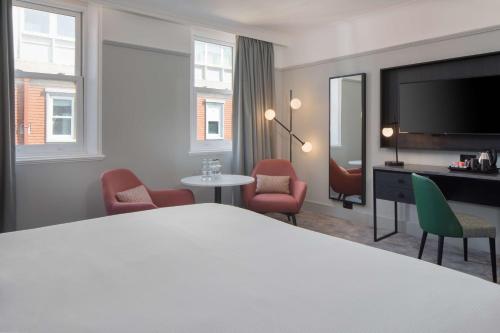 a hotel room with a bed and chairs and a television at DoubleTree By Hilton Brighton Metropole in Brighton & Hove