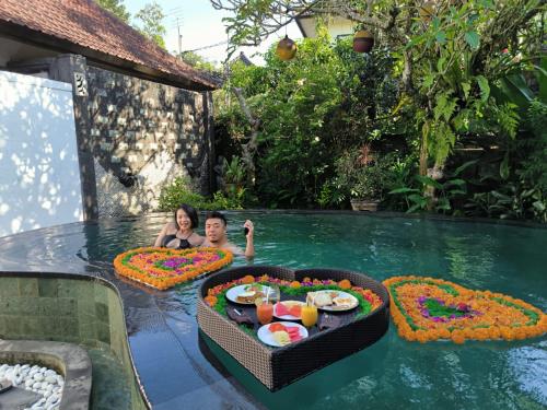 a man and woman swimming in a pool with flowers in the water at Baruna Sari Villa view jungle in Ubud