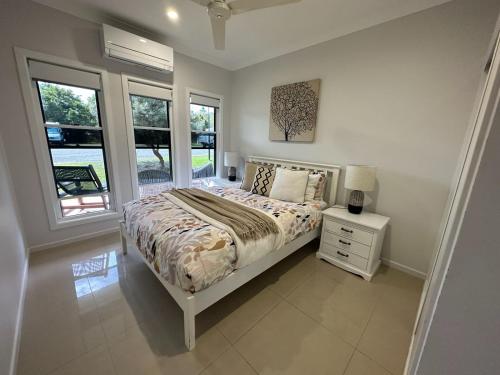 a bedroom with a bed with a nightstand and windows at Lily Pad Beach House in Agnes Water