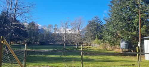 a fence in a field with trees and mountains at Coñaripe Kuyen Mapu Cabañas in Coñaripe