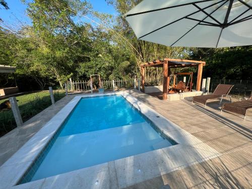 a swimming pool with an umbrella and a playground at Sítio Chalako, casa exclusiva às margens do Rio Mimoso in Bonito