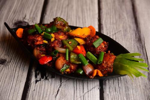 a black plate of food with vegetables on a wooden table at Hotel WB40 in Durgāpur