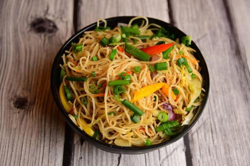a bowl of noodles with vegetables on a wooden table at Hotel WB40 in Durgāpur