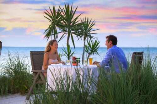 a man and woman sitting at a table on the beach at Bungalows at Windsong on the Reef in The Bight Settlements