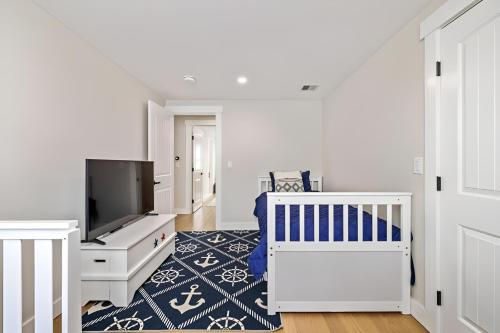 a white bedroom with a crib and a tv at Renovated & Sophisticated Home Near Beach & Shops! in Barnstable