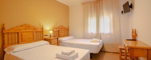 a bedroom with two beds and a desk and a television at Hostal Valdepeñas by Bossh Hotels in Valdepeñas