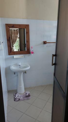 Baño blanco con lavabo y espejo en BBQ Lounge, en Dar es Salaam