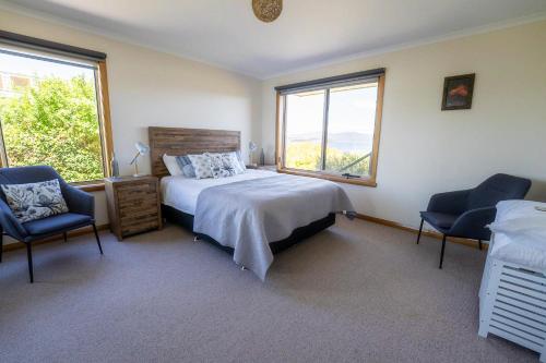 a bedroom with a bed and two chairs and two windows at Kiama Cottage beside the Bay in St Helens