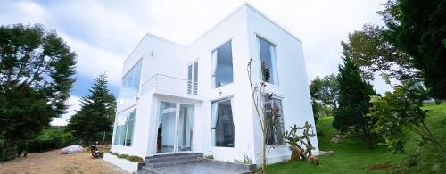 a white house with large windows on a field at Du Lịch Lâm Hà - Hồ Gia Trang Villas in Lam Ha