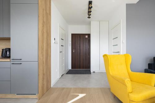 a living room with a yellow chair and a kitchen at Air-Conditioned Seaside Apartment with Parking & Balcony by Renters in Ustronie Morskie