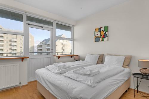 a bedroom with a bed with white sheets and windows at Baldursbrá Apartment Hverfisgata in Reykjavík